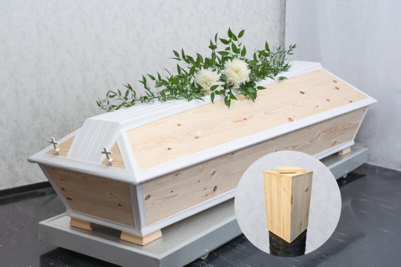 Hauta-arkku jossa on valkoista sekä vaaleaa puuta. Arkun päällä on kukkalaite. Kuvassa näkyy myös puinen uurna.